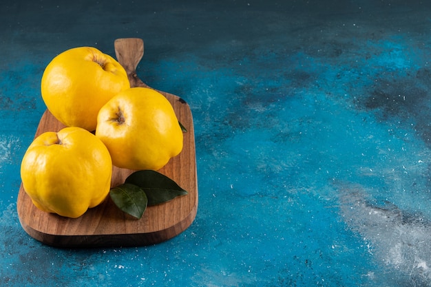 Tres frutos de membrillo amarillo colocados sobre tabla de madera