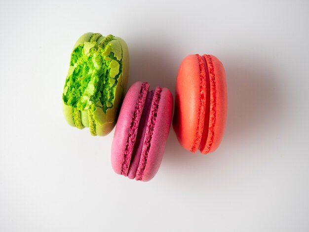 Tres galletas de macarrón sobre un fondo blanco. Uno de ellos está mordido. Vista superior, endecha plana