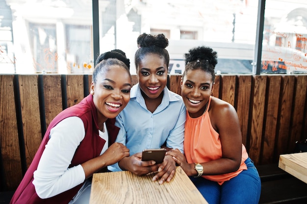 Três garotas afro-americanas sentadas na mesa de caffe e olhando no celular