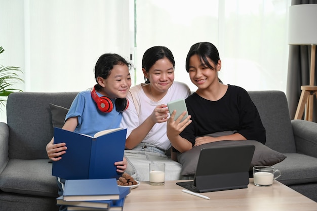 Três garotas assistindo algo engraçado no telefone inteligente enquanto sentam-se juntos no sofá da sala de estar.