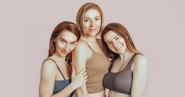 Três garotas em roupas confortáveis para casa juntas em um fundo rosa As mulheres sorriem e se divertem O conceito de tratamentos de spa beleza natural e cuidados creme de juventude e máscara de frescura amizade