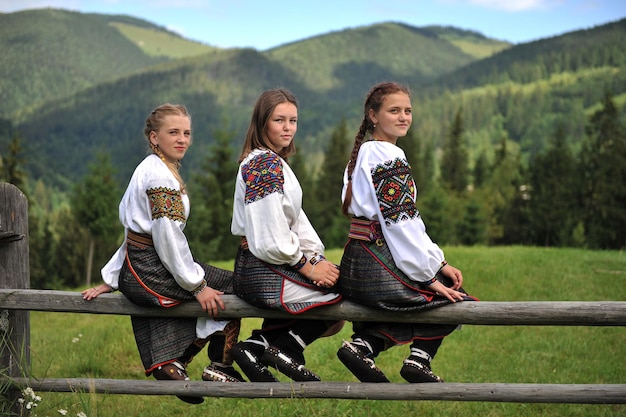 Três garotas ucranianas, vestidas com roupas Hutsul nacionais, estão sentadas em cima do muro.
