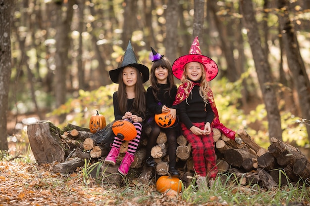 Três garotinhas em fantasias de bruxa de halloween riem e conjurem caminhada pela floresta de outono