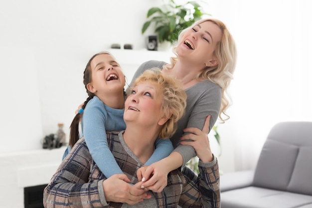 Tres generaciones de mujeres. Hermosa mujer y adolescente están besando a su abuela mientras están sentados en el sofá en casa