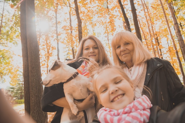 Tres generaciones de mujeres y perros se sienten divertidos mirando a la cámara posando juntos para una foto de autorretrato