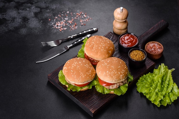 Três hambúrguer com hambúrguer de carne bovina e legumes frescos em fundo escuro