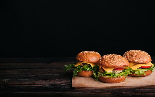 Tres hamburguesas caseras con carne, queso, lechuga, tomate en una mesa de madera