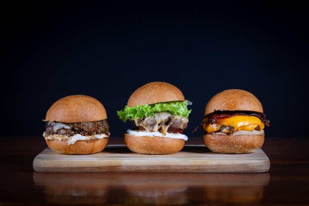 Foto tres hamburguesas colocadas en una tabla de madera hamburguesas muy sabrosas con queso derretido cheddar tocino lechuga tomate cebolla y salsa hamburgueses de carne artesanal hechos a mano