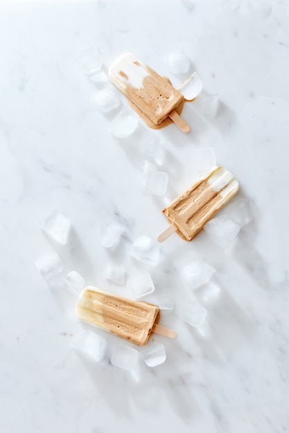Tres helados de café creme brulee en un palo de madera sobre fondo de mármol, vista superior. Postre de verano saludable