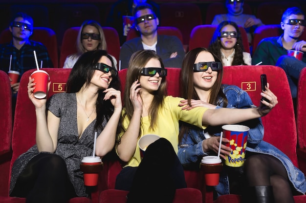 Foto tres hermosas amigas riendo felices haciendo una selfie juntos durante una película en el cine