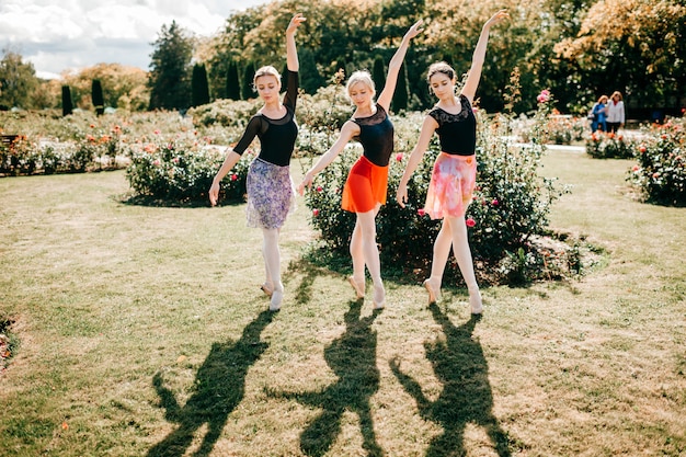 Tres hermosas bailarinas bailando y balanceándose sobre la luz del sol en el parque de verano