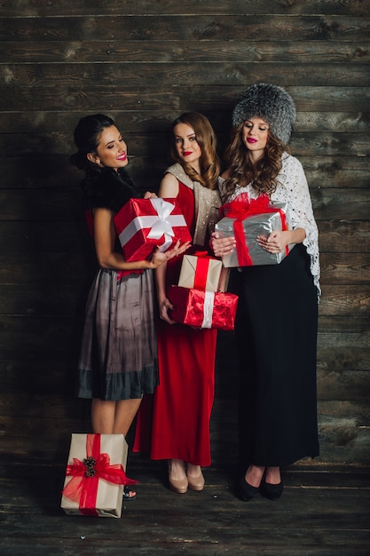 Tres hermosas chicas con regalos de Navidad en un fondo de madera