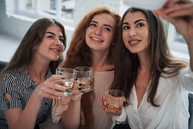 Tres hermosas chicas toman selfie con bebidas en sus manos