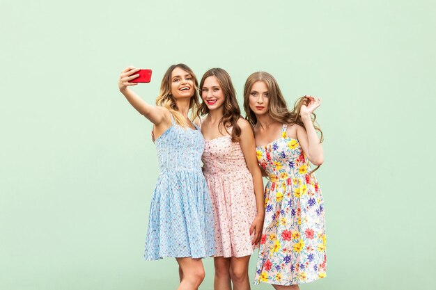 Tres hermosas hermanas en vestido macking selfie sobre fondo verde
