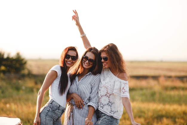 Foto tres hermosas mujeres jóvenes con gafas de sol de pie en el campo y sonriendo en un día soleado. .