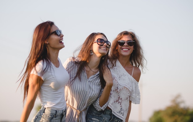 Tres hermosas mujeres jóvenes con gafas de sol vestidas con ropa hermosa se ríen al aire libre en un día soleado. .