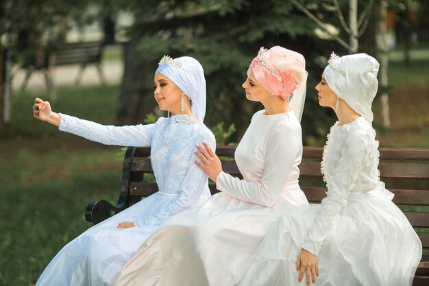 Tres hermosas mujeres jóvenes con vestidos musulmanes festivos toman una selfie en el teléfono