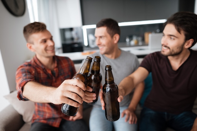 Tres hombres beben cerveza. Los chicos tienen botellas oscuras.