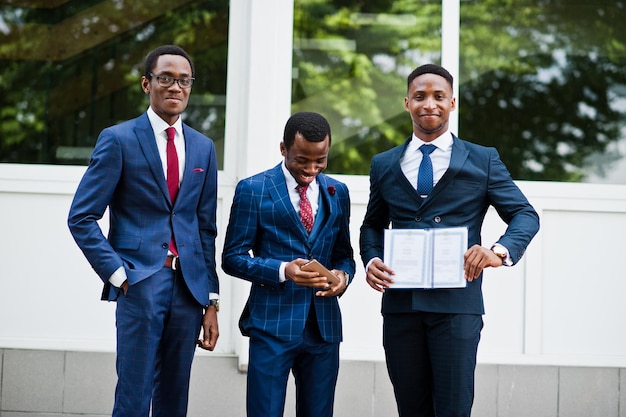 Tres hombres exitosos felices afroamericanos en traje con diploma en el día de la graduación