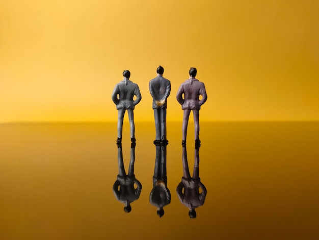 Foto tres hombres en miniatura con reflejo en un fondo amarillo