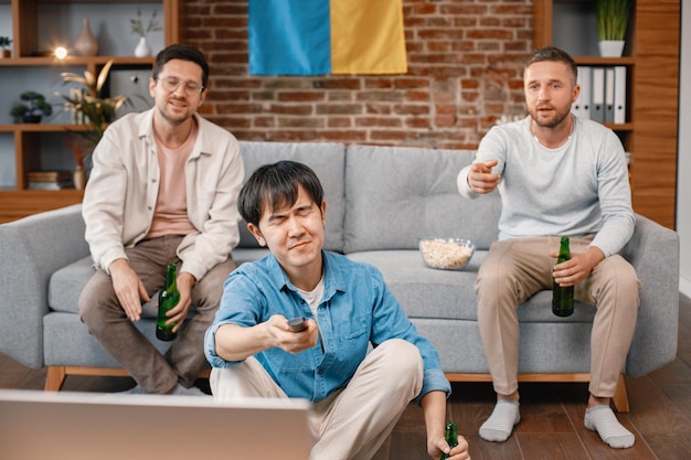 Tres hombres viendo un partido de fútbol en la televisión y bebiendo una cerveza