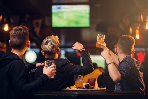 Três homens assistem futebol na TV em um bar esportivo, feliz lazer da companhia de fãs