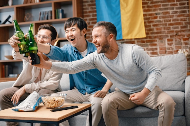 Três homens assistindo a um jogo de futebol na tv e bebendo uma cerveja