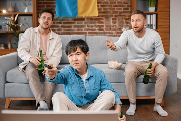 Três homens assistindo a um jogo de futebol na tv e bebendo uma cerveja