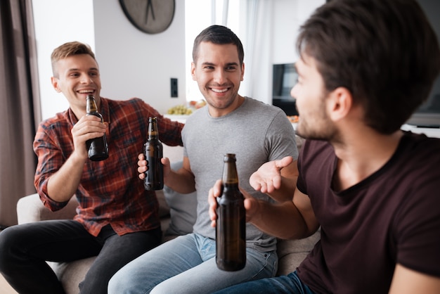 Foto três homens bebem cerveja de garrafas escuras.