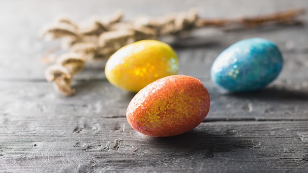 Tres huevos de colores y una rama de sauce sobre una mesa de madera oscura La decoración de la mesa de Pascua.