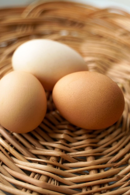 Tres huevos de gallina de diferentes colores y tamaños yacen en una cesta de mimbre