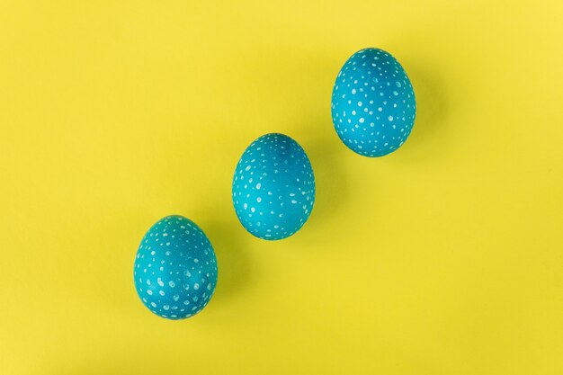 Tres huevos de Pascua azules sobre fondo amarillo brillante, vista superior