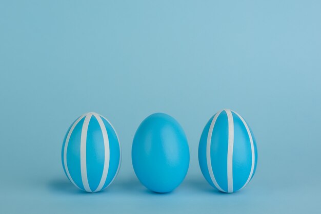 Tres huevos de Pascua decorados de azul. Rayas huevos azules en una fila sobre un fondo azul. Bandas blancas. Copia espacio Monocromo azul