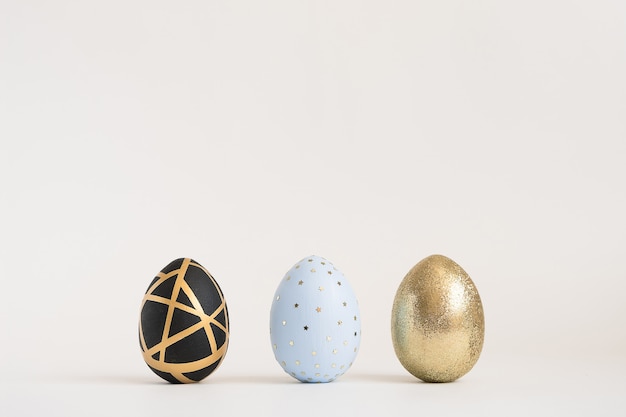 Tres huevos de Pascua decorados de oro sobre superficie azul. Concepto mínimo de pascua.