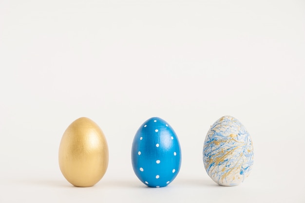 Tres huevos de Pascua decorados de oro sobre superficie azul. Concepto mínimo de pascua.