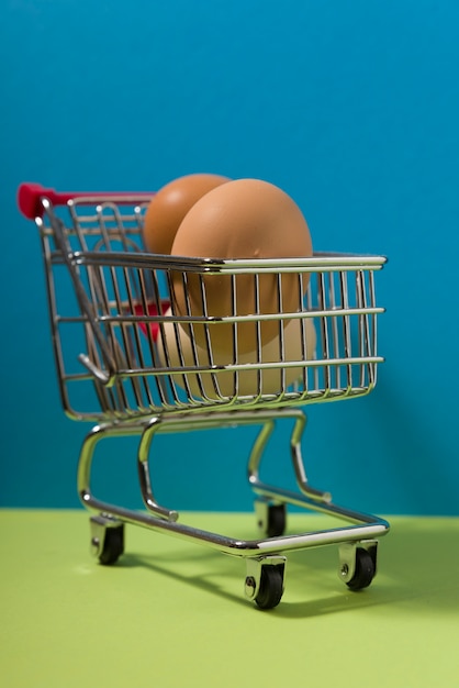 Tres huevos en un pequeño carrito de compras sobre fondo verde y azul