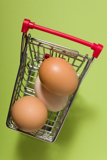 Tres huevos en un pequeño carrito de compras sobre fondo verde