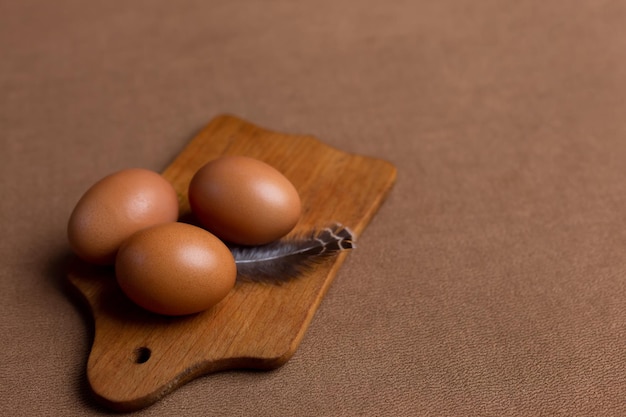 Tres huevos en una tabla de madera con una pluma sobre la mesa