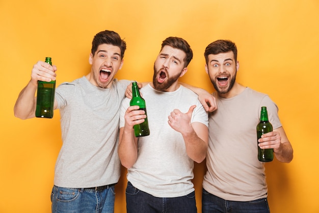 Tres jóvenes alegres sosteniendo cerveza y celebrando