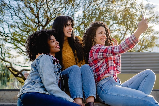 Tres jóvenes amigas estudiantes de intercambio multirraciales se toman una selfie en una escalera sonriendo