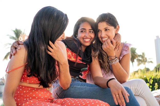 Tres jóvenes amigas latinas que tienen una conversación al aire libre en un día soleado de verano