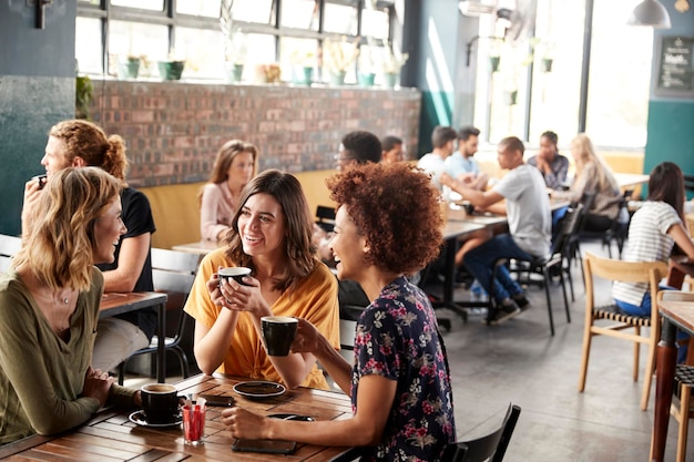 Tres jóvenes amigas reunidas sentarse a la mesa en la cafetería y hablar