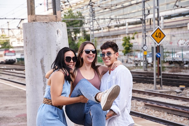 Tres jóvenes amigos divirtiéndose grupo de millennials llevando a una joven caucásica en sus brazos