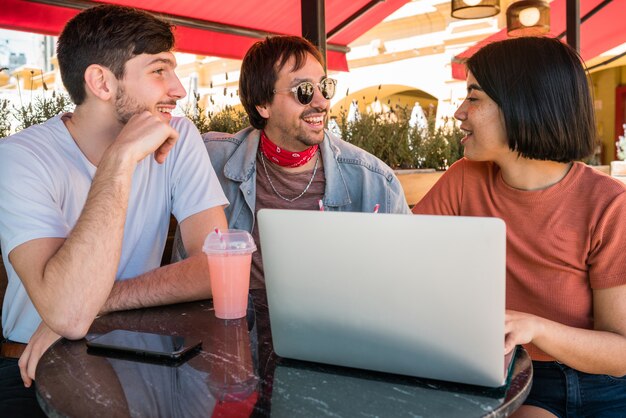 Tres jóvenes amigos usando la computadora portátil en la cafetería.