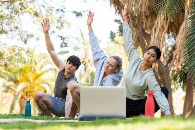 Tres jóvenes aprendiendo yoga y mirando la laptop Hay dos mujeres y un hombre