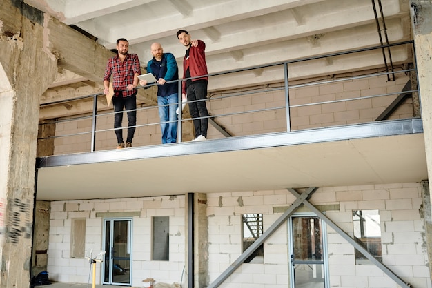 Foto uno de los tres jóvenes arquitectos apuntando a la esquina del edificio sin terminar durante la discusión de nuevos materiales en la reunión de puesta en marcha