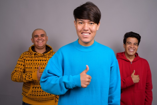Foto tres jóvenes asiáticos vistiendo ropa de abrigo contra la pared gris