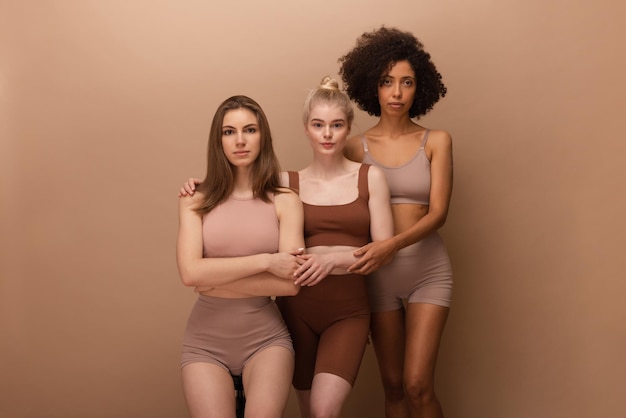 Tres jóvenes chicas interraciales agradables con cabello oscuro y rubio miran penetrantemente a la cámara sobre fondo beige