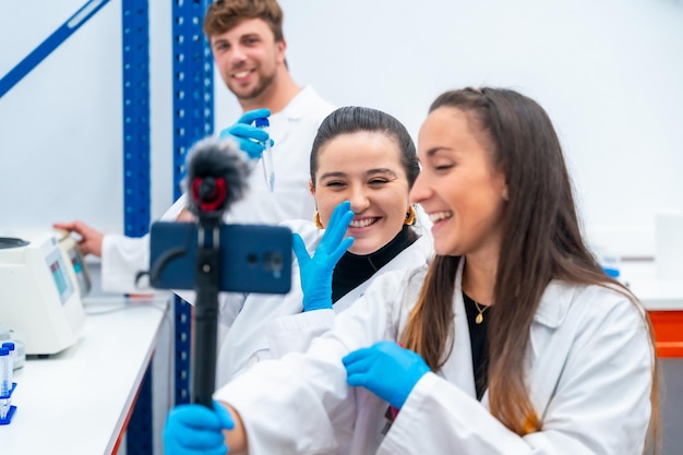 Foto tres jóvenes científicos transmitiendo un video en vivo dentro de un laboratorio de investigación