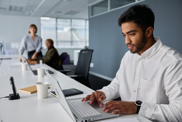 Tres jóvenes empresarios multirraciales en ropa de negocios trabajando en computadoras portátiles en el escritorio de la oficina
